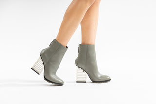 United Nude, Hi Rise, Grey leather boot with zip and sole tread and a clear see through heel modelled with feet and legs, The Shoe Curator