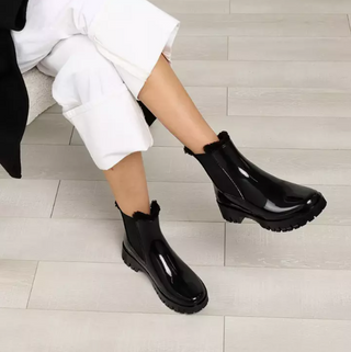 Lemon Jelly, Colden Black, Black patent ankle gum boot with thick gripped outer sole and a fluffy inside styled with white pants and modelled on feet and legs, The Shoe Curator