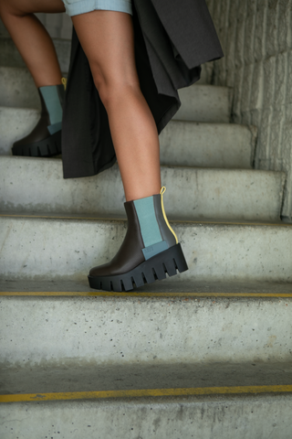 United Nude brown leather platform boot with yellow and blue features, paired with blue shorts and black jacket on concrete stairs