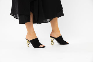 Kat Maconie, Kylie, black suede front cover on a peeped toe high heel with a twisted gold patent heel syled with long black dress modelled with legs and feet, The Shoe Curator