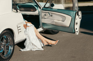 Billini, Preach, White leather strappy with with small silver buckle and pointed toes with stiletto heel styled with white dress in car and modelled with feet and legs, The Shoe Curator
