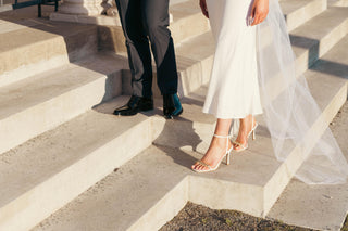 Billini, Blane, White leather stiletto with thin ankle strap and thin toe band with gold loop chain styled with white dress and modelled with feet and legs, The Shoe Curator