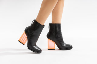 United Nude, Hi Rise, Black leather patent boot with zip and black sole thread with a see through orange heel modelled with feet and legs, The Shoe Curator