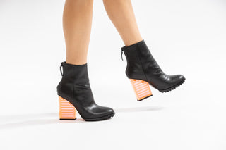 United Nude, Hi Rise, Black leather patent boot with zip and black sole thread with a see through orange heel modelled with legs and feet, The Shoe Curator
