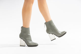 United Nude, Hi Rise, Grey leather boot with zip and sole tread and a clear see through heel modelled with legs and feet, The Shoe Curator