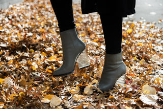 United Nude, Hi Rise, Grey leather boot with zip and sole tread and a clear see through heel styled with leggings and coat next to autumn leaves modelled on legs and feet, The Shoe Curator