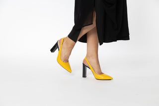 Capelli Rossi yellow high heel with a slingback strap and pointed toes with a black patent block pump heel styled with a long black dress modelled with feet and legs, Arla, The Shoe Curator.