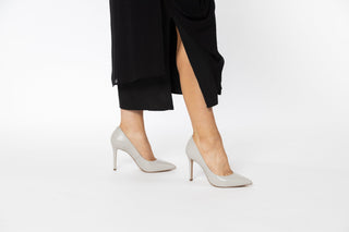 Capelli Rossi White patent stiletto with pointed toes styled with a long flowy black dress modelled with legs and feet, Katie, The Shoe Curator