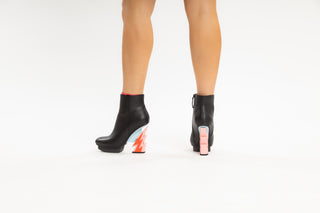 United Nude, Glam Bootie, Black patent ankle boot with pink and red lightning bolt heel with silver stability modelled with feet and legs, The Shoe Curator