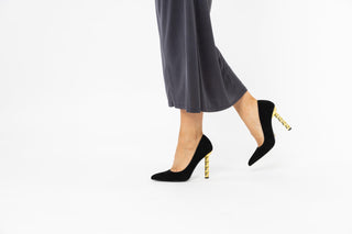 Kat Maconie, Lydia, Black suede stiletto with pointed toes and a twisted gold chain heel styled with dark grey dress and modelled with feet and legs, The Shoe Curator