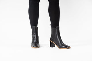 Gioseppo, Yala, Black leather ankle boot with pointed toes and brown rubber sole with elastic chunk and sharp edged block heel styled with sheer black pants and modelled with feet and legs, The Shoe Curator