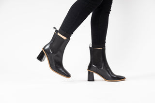 Gioseppo, Yala, Black leather ankle boot with pointed toes and brown rubber sole with elastic chunk and sharp edged block heel styled with black jeans and modelled with feet and legs, The Shoe Curator