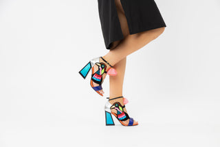 Kat Maconie, Aya, Blues and pinks leather pump with block heel and pop pom detailing and peeped toe and bird design out of tassels and sequences with adjustable ankle strap styled with black open dress and modelled with feet and legs, The Shoe Curator
