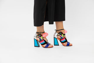 Kat Maconie, Aya, Blues and pinks leather pump with block heel and pop pom detailing and peeped toe and bird design out of tassels and sequences with adjustable ankle strap styled with black dress and modelled with legs and feet, The Shoe Curator