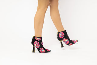 Kat Maconie, Lucie, Ankle boot with suede black and colourful flower designs with pointed toes and a zip on the back, hourglass black heel with gold edging modelled with feet and legs, The Shoe Curator