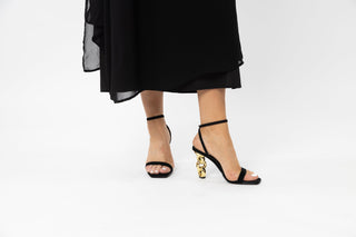 Kat Maconie, Riri, Navy blue suede with thins strap over peeped toe and thin adjustable ankle strap with gold patent chain heel styled with black dress and modelled with legs and feet, The Shoe Curator