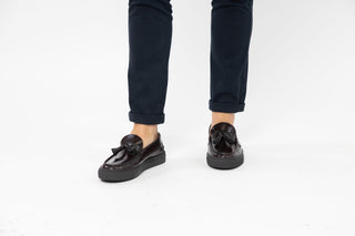 Ted Baker, Petie, Brown patent loafers with tassels on the front and stitching details styled with jeans and modelled with feet and legs, The Shoe Curator