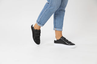 Ted Baker, Tayree, Black leather sneakers with 3 velcro straps on the top and with white detailing styled with jeans and modelled with feet and legs, The Shoe Curator