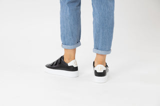 Ted Baker, Tayree, Black leather sneakers with 3 velcro straps on the top and with white detailing styled with jeans and modelled with feet and legs, The Shoe Curator