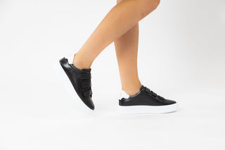 Ted Baker, Tayree, Black leather sneakers with 3 velcro straps on the top and with white detailing modelled with feet and legs, The Shoe Curator