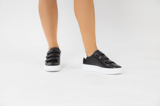 Ted Baker, Tayree, Black leather sneakers with 3 velcro straps on the top and with white detailing modelled with feet and legs, The Shoe Curator