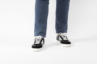 Ted Baker, Robbert, Black leather sneakers with white detailing and white laces styled with jeans and modelled with feet and legs, The Shoe Curator