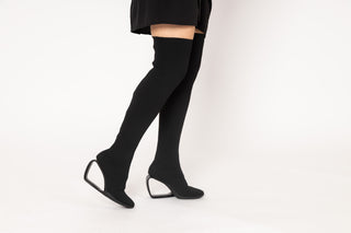 United Nude, Mobius Long Boot Hi, Black mid thigh boot with black stretchy material, heel with a thin piece creating a hollow middle styled with black mini dress modelled with feet and legs, The Shoe Curator